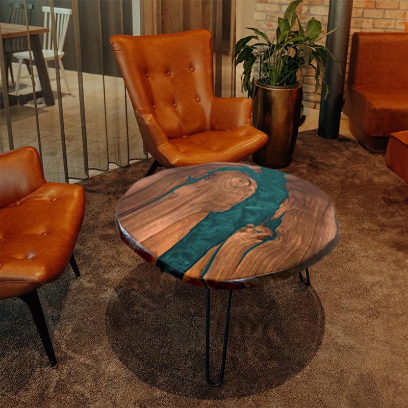 Couchtisch rund mit Naturkanten aus Nussbaum & Epoxidharz in türkis, in gemütlichem Setting mit zwei braunen Ledersesseln. Modell Titisee von schwarzhirsch