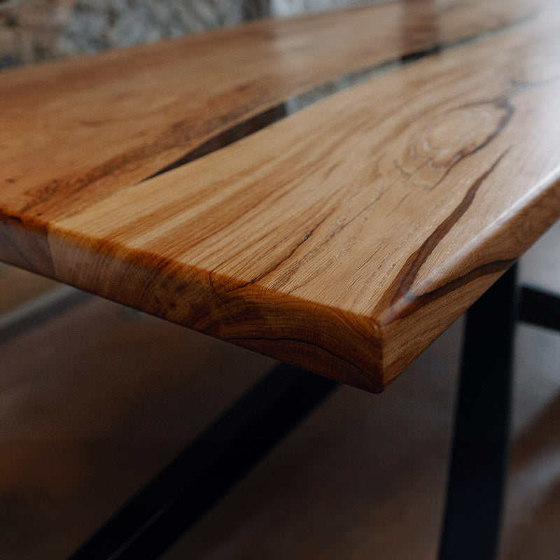 River Table. Detailbild der geraden Baumkante des Esstischs aus Eiche. Modell Feldberg mit Kreuzgestell von Schwarzhirsch