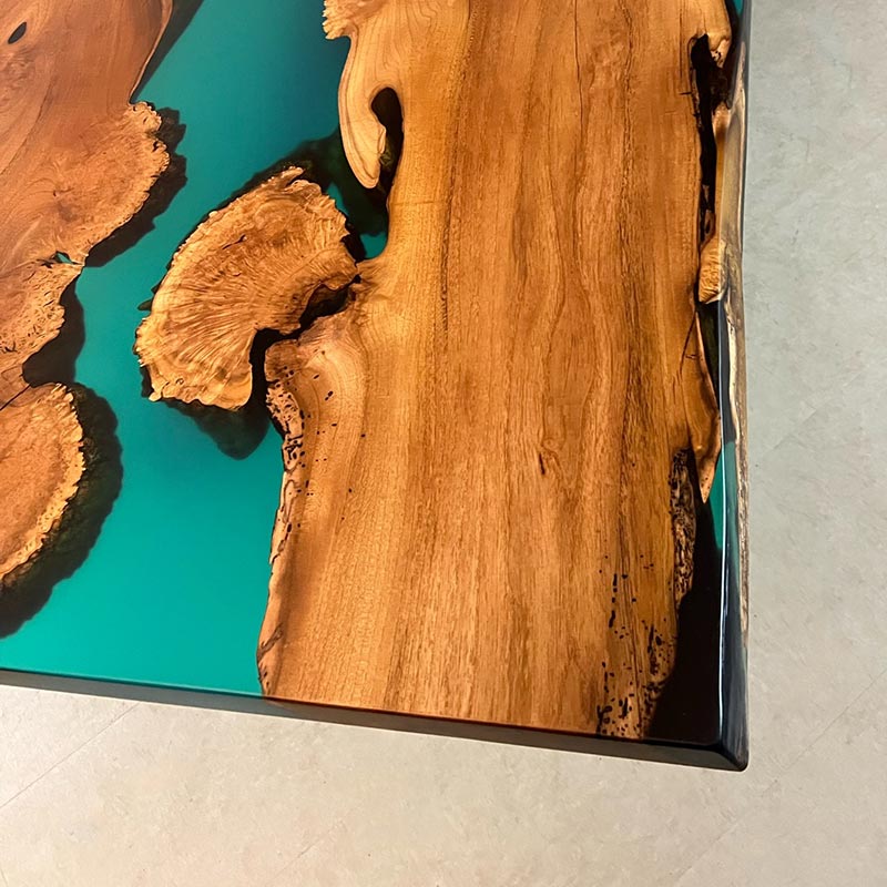 Tischkante mit türkis-blauem Epoxidharz an natürlicher Baumkante von Epoxidharz Tisch aus Akazie mit Kreuzgestell. Modell Gletschersee von Schwarzhirsch