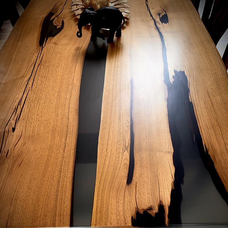 Epoxidharz Tisch. Detailbild der Oberfläche von einem Esstisch aus Akazie mit grau-transparentem Epoxidharz. Modell Kuckuck Nummer 2 mit Spidergestell von schwarzhirsch