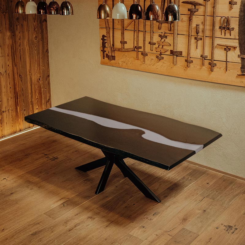 River Table. Esstisch schwarze Eiche mit weißem Epoxidharz und Kreuzgestell. Modell Blackforest von Schwarzhirsch