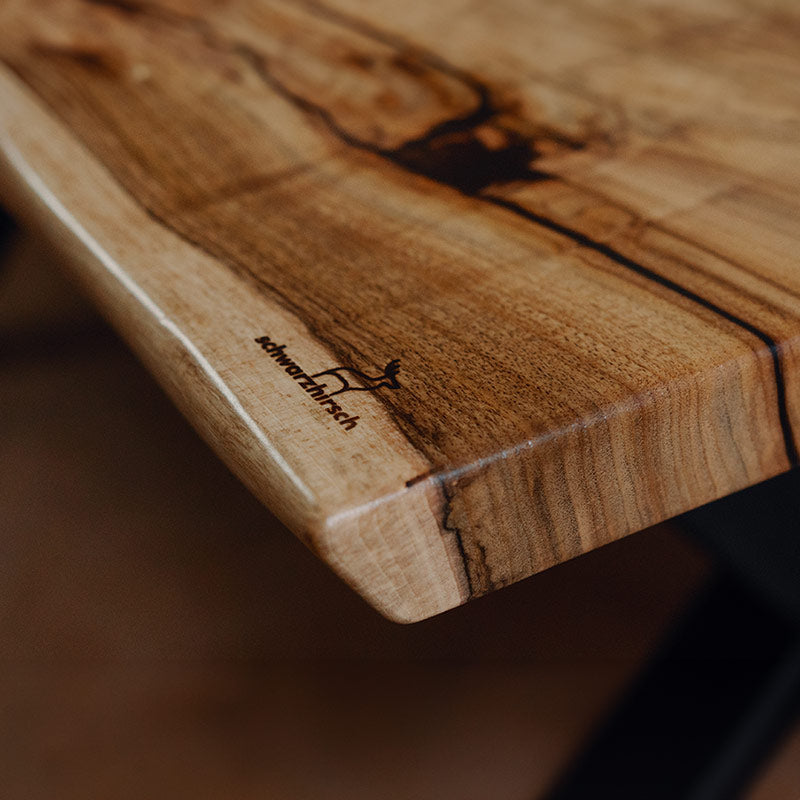 Epoxidharz Tisch. Baumkante mit Logo-Brennstempel von Epoxidharz Tisch aus Nussbaum schwarz mit  X-Gestell. Modell Wutachschlucht von schwarzhirsch