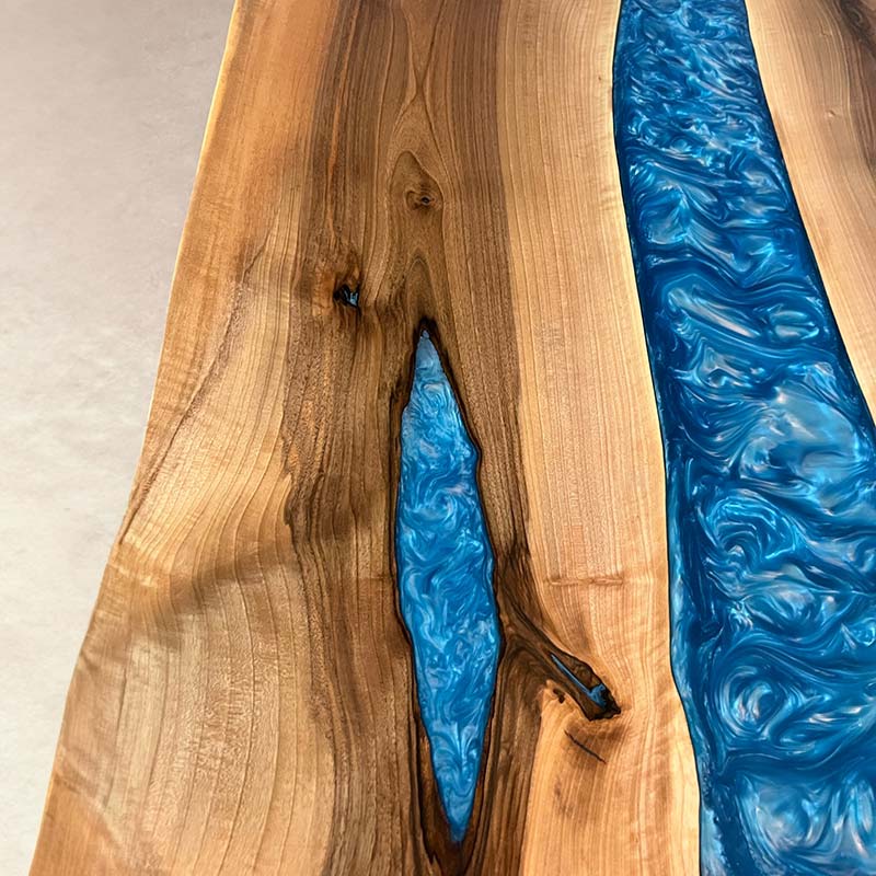 Detailbild Oberfläche und Farbverlauf von Epoxidharz Tisch aus Nussbaum mit blau pigmentiertem Epoxidharz. Modell Kinzig mit Kreuzgestell von Schwarzhirsch
